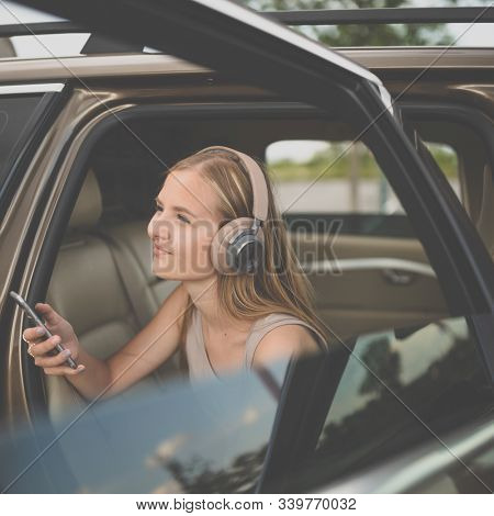 Cute teenage girl listening to her favorite music/audiobook on hig-end headphones during a roadtrip