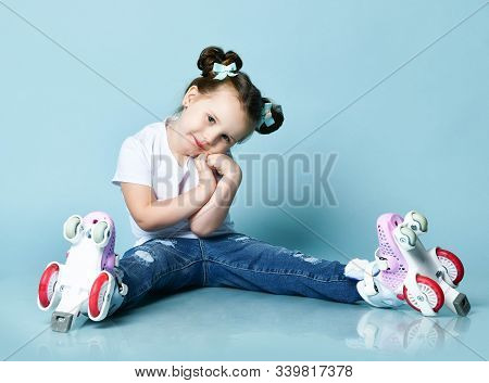 Kid Girl With Funny Buns In T-shirt And Blue Jeans Is Sitting With Roller Skates On Her Feet, Nice P