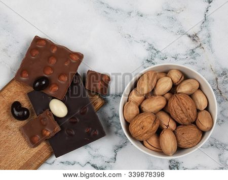 Broken Chocolate Bars, Raw Inshell And Chocolate Covered Nuts On Gray Marble Background. Top View Wi
