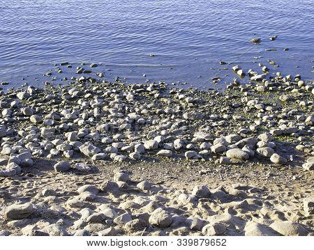The River Bank, The Sea Covered With Pebbles. Stone Shore And Water