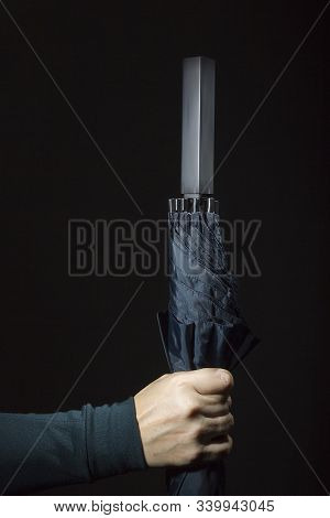 Female Hand With Folded Umbrella On A Black Background