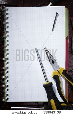 Screwdriver And Pliers On A Checkered Notebook