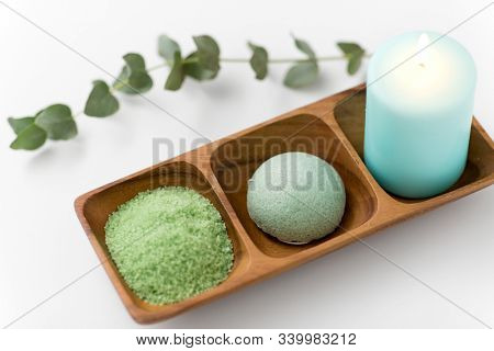 beauty, spa and wellness concept - green bath salt, konjac sponge and candle on wooden tray with eucalyptus cinerea