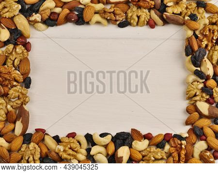 Walnut Frame. Different Nuts And Raisins On A White Wooden Background Are Laid Out In The Form Of A 