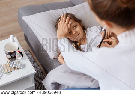 Indoor Shot Of Little Girl Lying On Sofa, Doctor Using Stethoscope On To Examine Kids Lungs, Child C