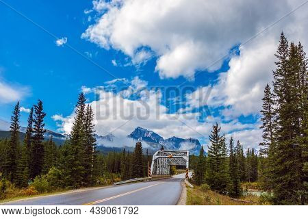 Trellised bridge across the river. Cloudy fall day in the Canadian Rockies. Evergreen forest grows along the side of the road. Concept of active, eco and photo tourism