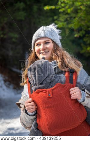 Young Smiling Babywearing Mother With Her Baby In Sling Winter Walking.