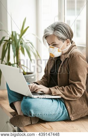 Greying Businesswoman Works Laptop From Home. Aged Woman Wearing Protective Mask Uses Mobile Interne
