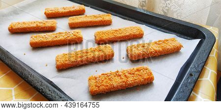 Frozen fish sticks are laid out on baking paper. Cooking a fish delicacy. Baking paper on a baking s