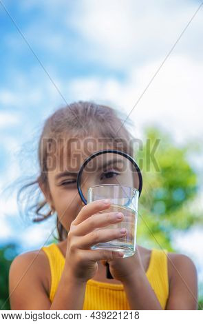 The Child Examines A Glass Of Water With A Magnifying Glass. Selective Focus.