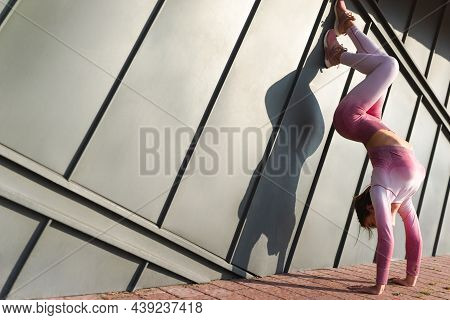 Athetic Girl Doing Handstand Against The Wall On The Street