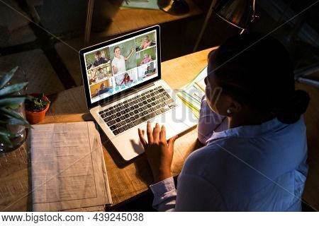 African american woman using laptop for video call, with diverse elementary school pupils on screen. communication technology and online education, digital composite image.