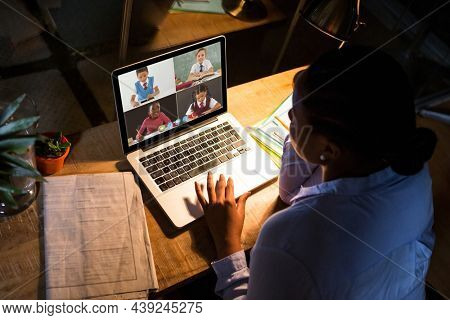 African american woman using laptop for video call, with diverse elementary school pupils on screen. communication technology and online education, digital composite image.