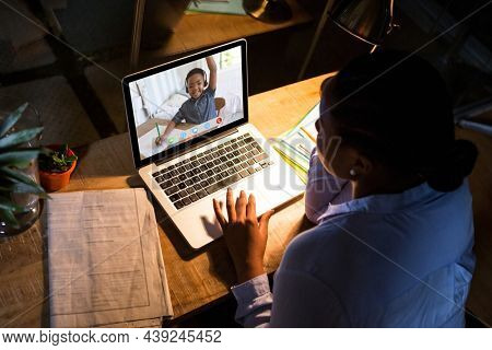 African american woman using laptop for video call, with elementary school pupil on screen. communication technology and online education, digital composite image.