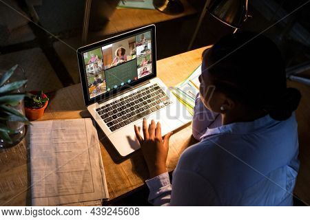 African american woman using laptop for video call, with diverse elementary school pupils on screen. communication technology and online education, digital composite image.