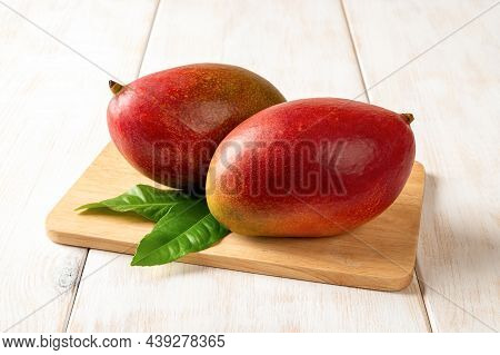 Two Red Ripe Palmer Mangoes On A Cutting Board Over White Wooden Table. Ready To Eat Whole Sweet Tas