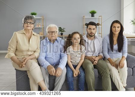 Multi Generational Family Sitting On Sofa At Home And Watching Television Together