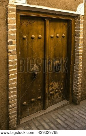 Yazd, Iran, February 19, 2021:a Double-leaf Wooden Entrance Door, Framed By Bricks, On The Wall Of A