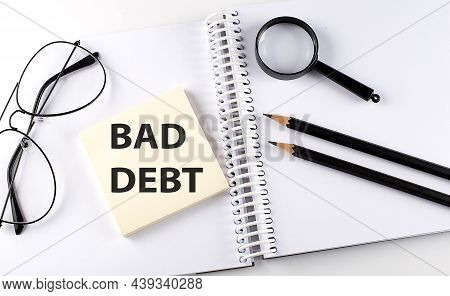 Word Bad Debt On The Sicker On The Notebook With Pencils,magnifier And Glasses