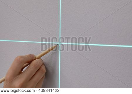 Woman Using Cross Line Laser Level And Pencil For Accurate Measurement On Grey Wall, Closeup