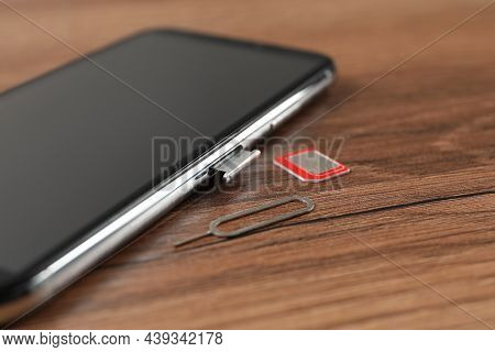Mobile Phone, Sim Card And Ejector Tool On Wooden Table, Closeup