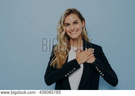Blonde Positive Young Female In Black Coat Showing Her Appreciation And Gratitude By Placing Hands O