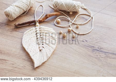 Macrame Leaf  In Natural Color And Thread Windings Lying On A Wooden Table. Cotton Rope Decor Macram