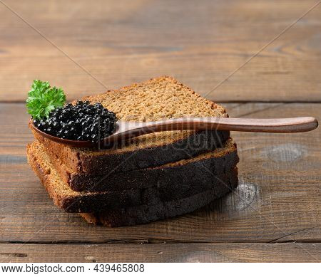 Fresh Grainy Black Paddlefish Caviar And Slices Of Bread In Brown Wooden Spoon On A Brown Table, Clo