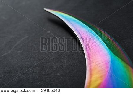 The Curved Sharp Blade Of The Kerambit Dagger Is A Gradient Rainbow Color On A Dark Background.