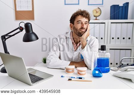Young hispanic dentist man working at medical clinic thinking looking tired and bored with depression problems with crossed arms. 