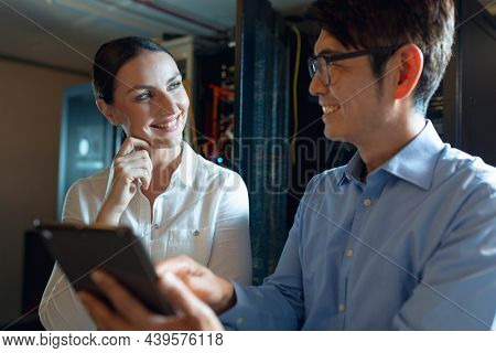 Diverse male and female engineers smiling while using digital tablet in computer server room. database server management and maintenance concept
