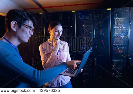 Diverse male and female engineers using laptop in computer server room. database server management and maintenance concept