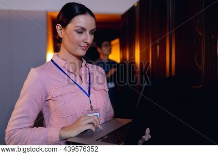 Caucasian female engineer using laptop in computer server room. database server management and maintenance concept