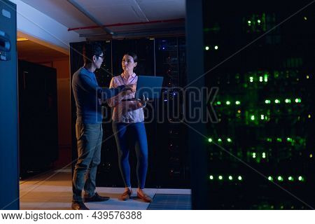 Diverse male and female engineers using laptop in computer server room. database server management and maintenance concept