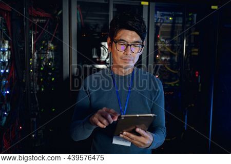 Asian male engineer using digital tablet in computer server room. database server management and maintenance concept