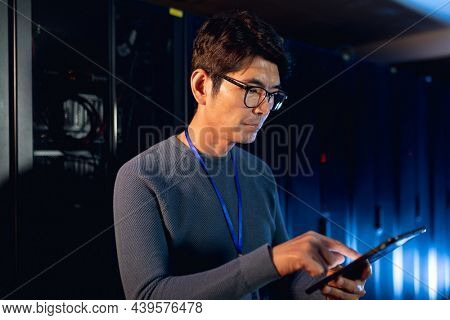 Asian male engineer using digital tablet in computer server room. database server management and maintenance concept