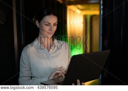 Caucasian female engineer using laptop in computer server room. database server management and maintenance concept