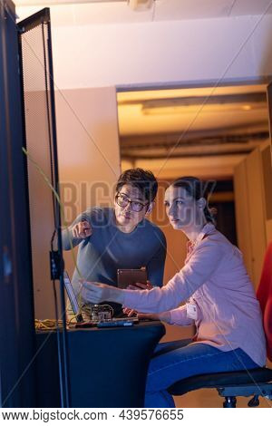 Diverse male and female engineers discussing over a digital tablet while inspecting in server room. database server management and maintenance concept