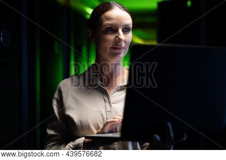 Caucasian female engineer using laptop in computer server room. database server management and maintenance concept