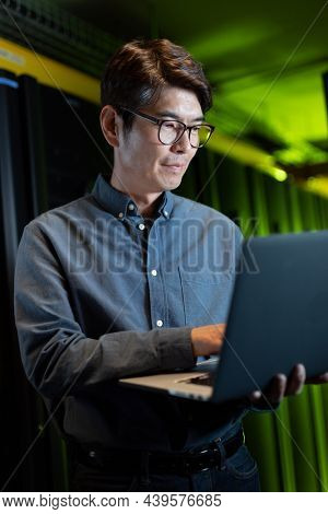 Asian male engineer using laptop in computer server room. database server management and maintenance concept