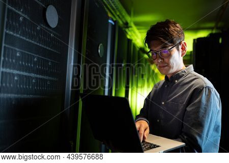 Asian male engineer using laptop in computer server room. database server management and maintenance concept