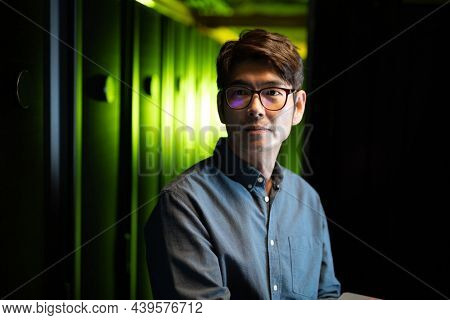 Asian male engineer using laptop in computer server room. database server management and maintenance concept