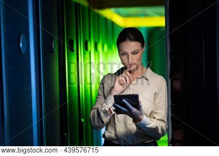 Thoughtful caucasian female engineer using digital tablet in computer server room. database server management and maintenance concept