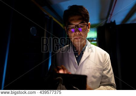 Asian male engineer wearing an apron using digital tablet in computer server room. database server management and maintenance concept