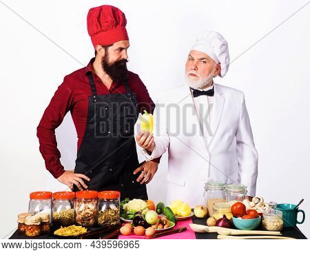Two Chefs In Uniform Stands Near Table With Vegetable. Chef With Assistant In Kitchen Ready To Cook.