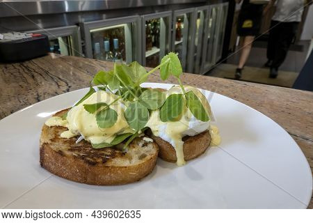 Eggs Benedict On Sourdough Toast On A White Plate And Topped With Greens
