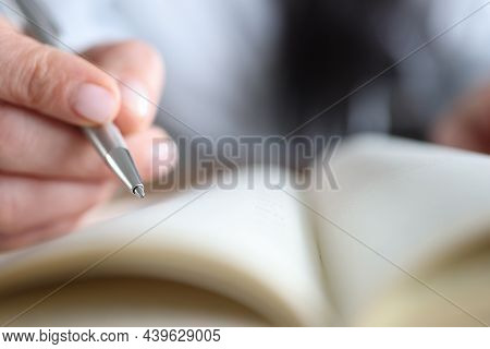A Womans Hand Holds A Pen Near A Notepad Close-up, Blurry. Document Signature, Synopsis, Research An