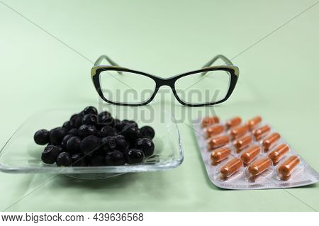 Natural Blueberries, Vitamin Capsules For Improving Vision And Eyeglasses On A Green Background.