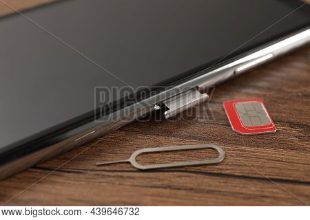 Sim Card, Mobile Phone And Ejector Tool On Wooden Table, Closeup