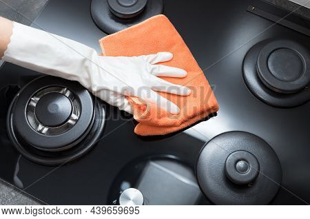 Person Hand In Rubber Glove Holding Rag And Wiping Gas Stove Top. House Cleaning Concept. Top View